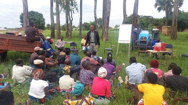 Eine Gruppe von Teilnehmenden werden auf einer Waldlichtung sitzend zu Vorteilen eines neuen Agrorforstmodells in Sambia geschult.